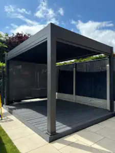 Modern dark grey aluminium pergola with slatted side panels, blending seamlessly into a garden space.