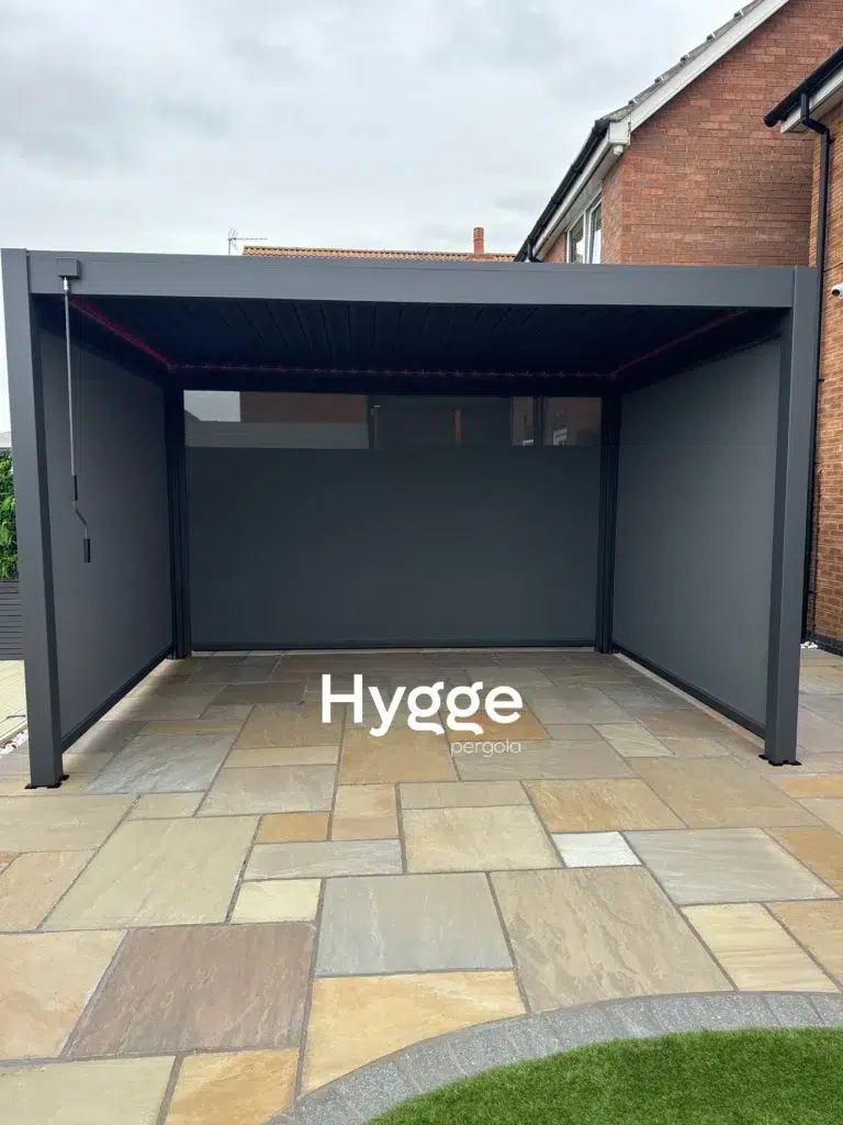 Enclosed dark grey aluminium pergola with integrated lighting, creating a cosy outdoor living space.